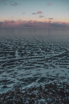 Captivating view of a frozen lake with unique ice patterns at dusk, under a pastel sky.