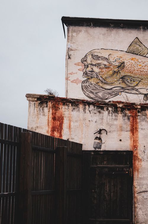 Free An artistic mural depicting a face and fish on a weathered building wall, enhancing urban aesthetic. Stock Photo
