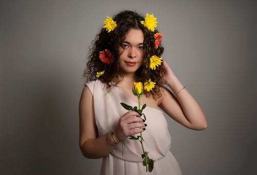 Free Charming studio portrait of a woman with curly hair adorned with colorful flowers, holding a rose. Stock Photo