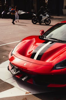 Close-up of a red Ferrari with racing stripes parked outdoors on pavement.