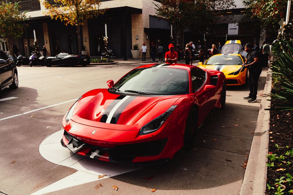 Red Ferrari sports car showcased at an exciting public car show event with people admiring luxury vehicles.
