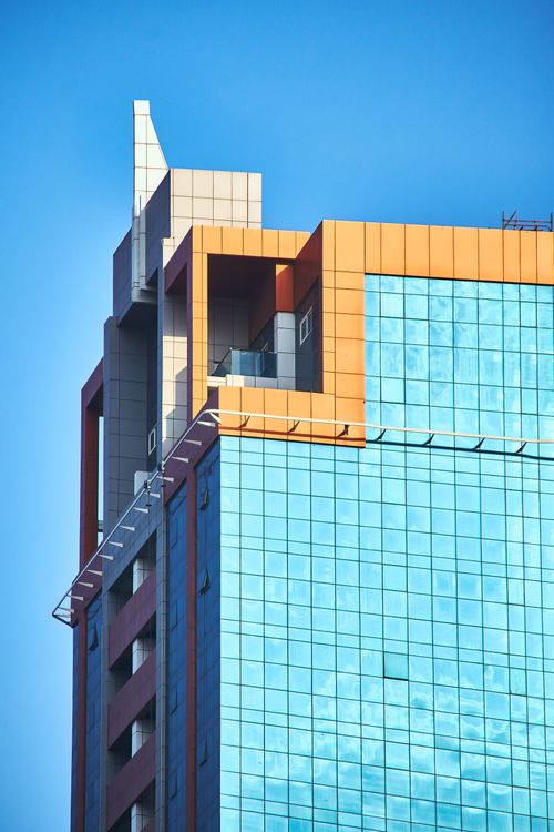 Free A striking modern skyscraper showcases geometric architecture with reflective glass windows against a blue sky. Stock Photo
