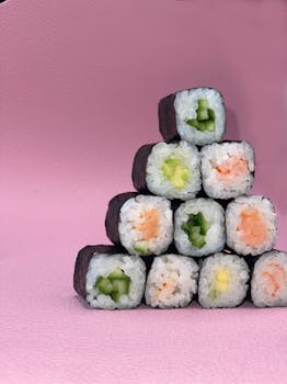 Stacked sushi rolls with various fillings on a pink background.