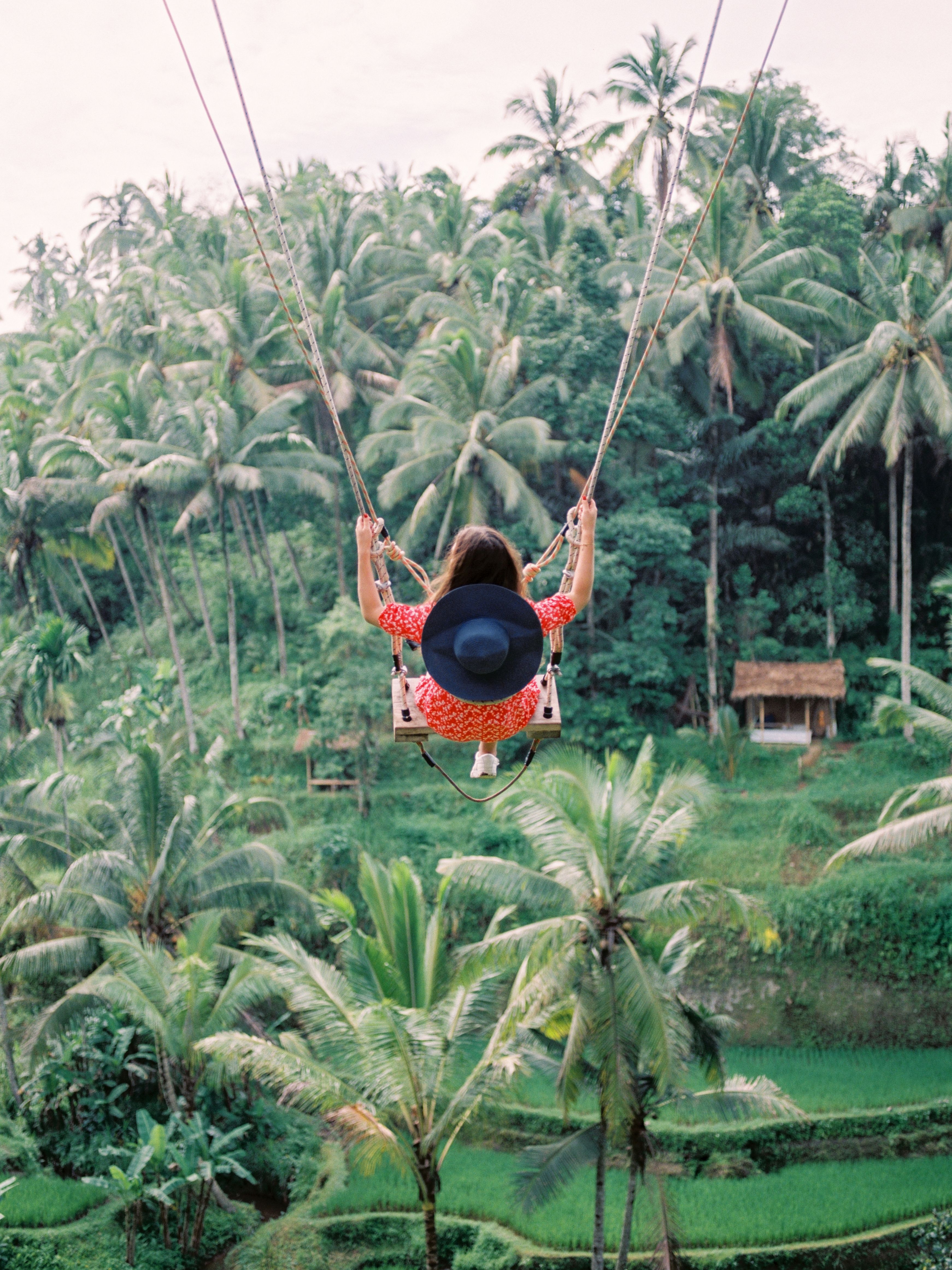 Solo female traveller mid-swing in flowing dress over the Ayung River valley at Real Bali Swing in Ubud, with jungle canopy and rice terraces visible below