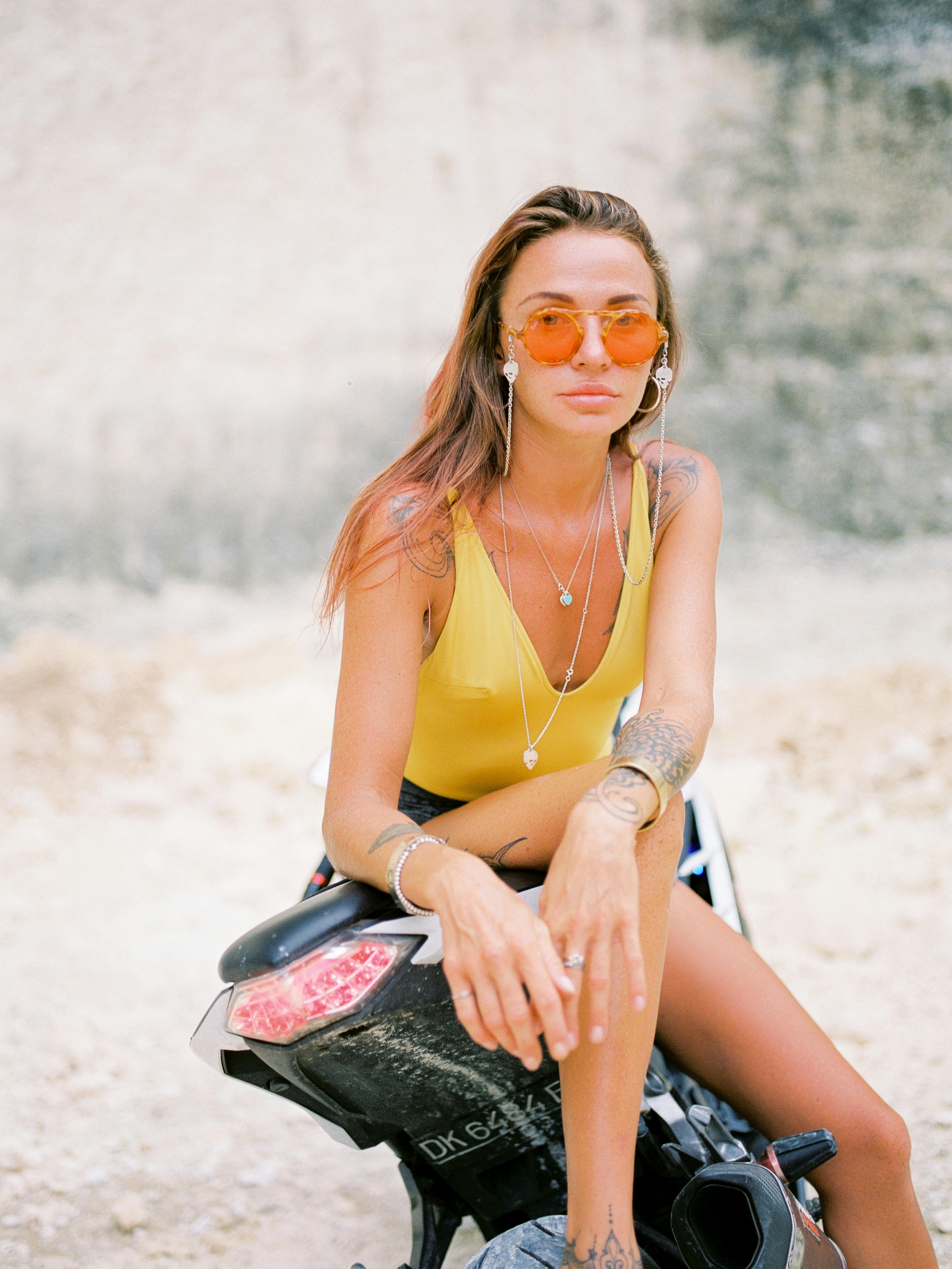 Fashionable woman posing on a motorcycle in Bali, wearing sunglasses and jewelry.