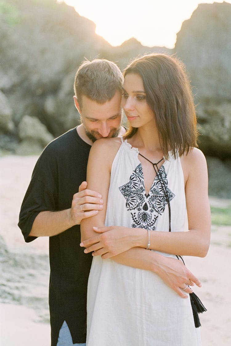 Young Man Standing Behind His Girlfriend And Kissing Her In Shoulder