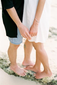 A romantic couple standing barefoot on a sandy beach in Bali, holding hands intimately.