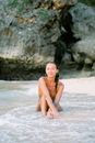 Smiling Young Woman in Bikini Sitting in Water at Seashore