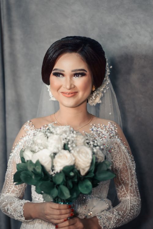 Free A beautiful Asian bride with a white rose bouquet, smiling on her wedding day in an elegant gown. Stock Photo
