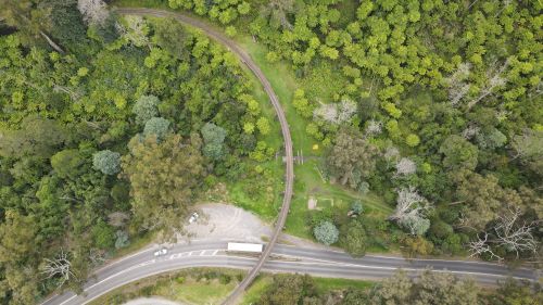 Free Aerial view of scenic railway tracks and road amidst lush green forest in Belgrave, VIC, Australia. Stock Photo