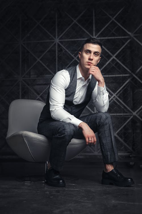 Free A Man in White Long Sleeve Shirt and Gray Pants Sitting on Gray Leather Chair Stock Photo
