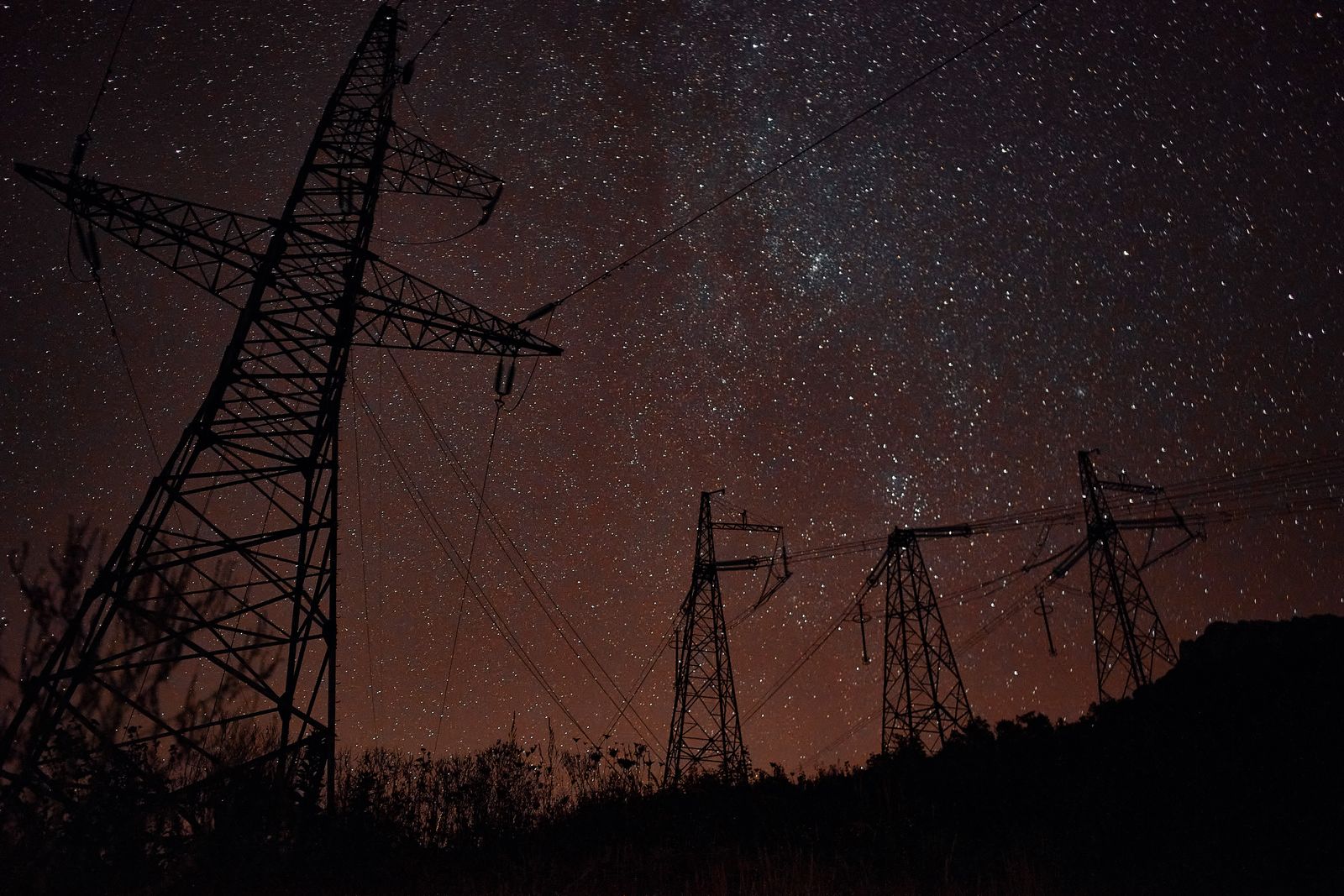 Transmission towers silhouetted against a star-filled night sky — photo by Artem Korsakov on Pexels