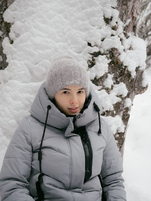 Free A woman in a warm jacket and woolen hat poses against a snowy tree in winter. Stock Photo