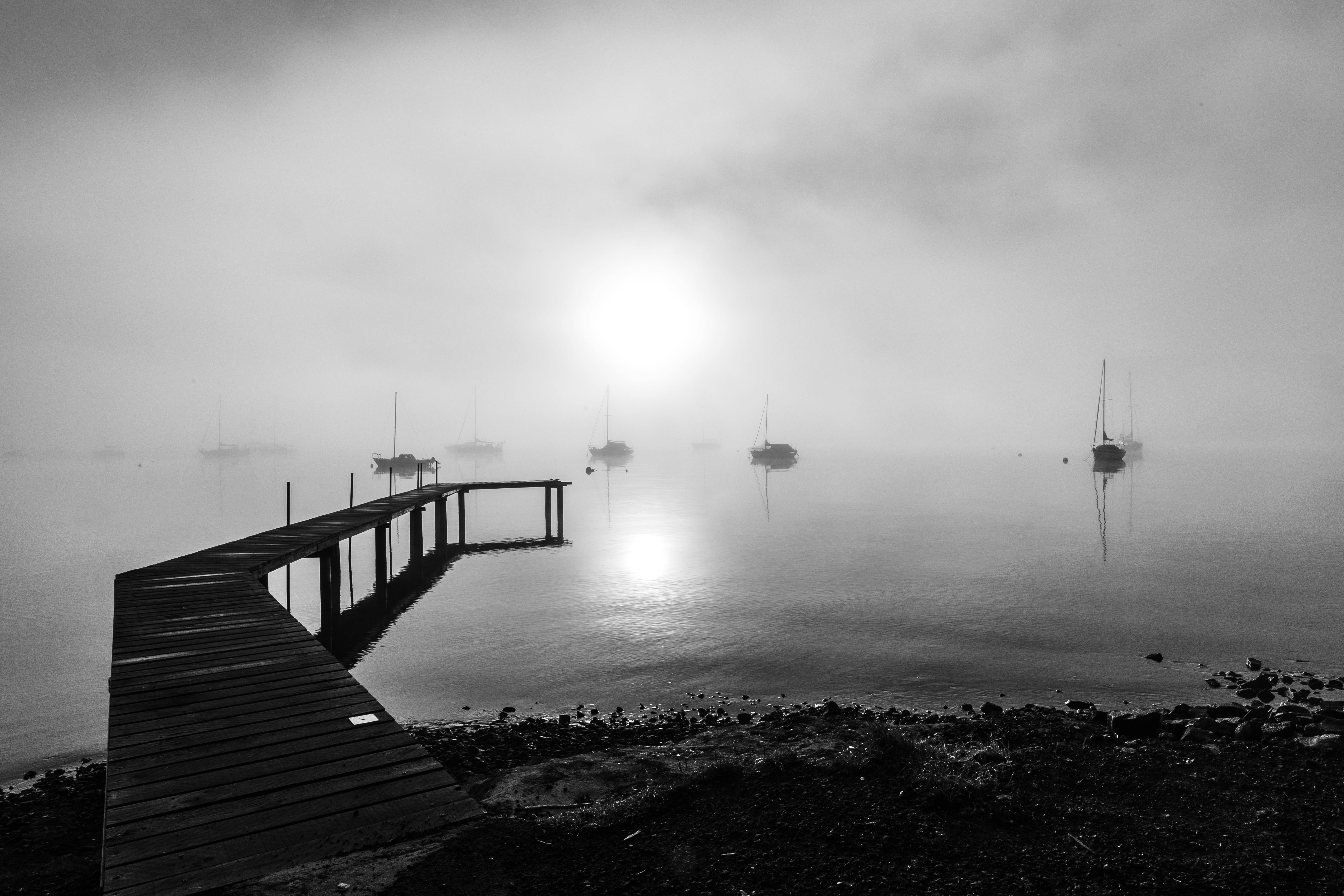 Black and white seascape of a foggy morning with boats by a wooden dock in Tasmania.