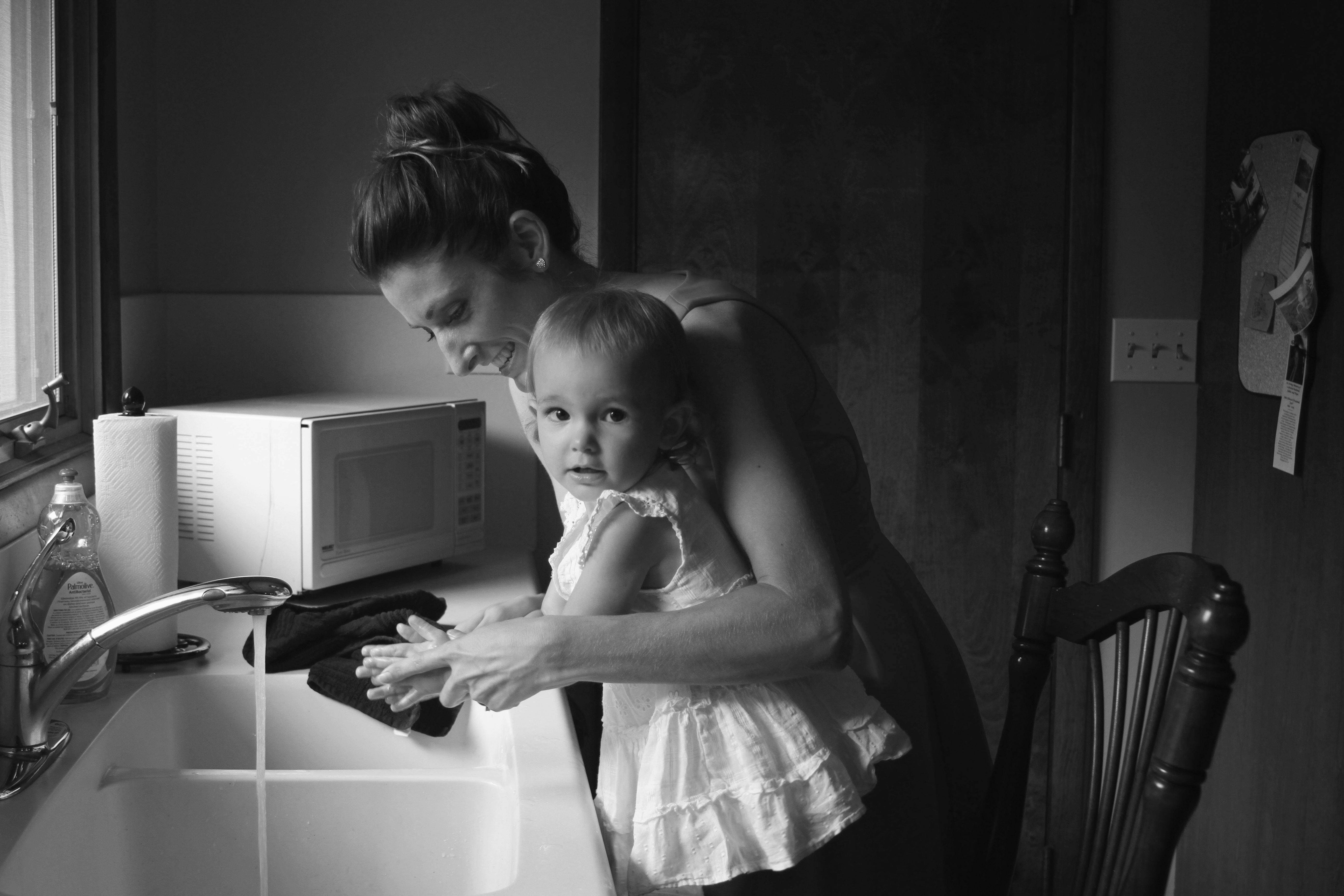 grayscale photography of mother helping her baby to wash her hands