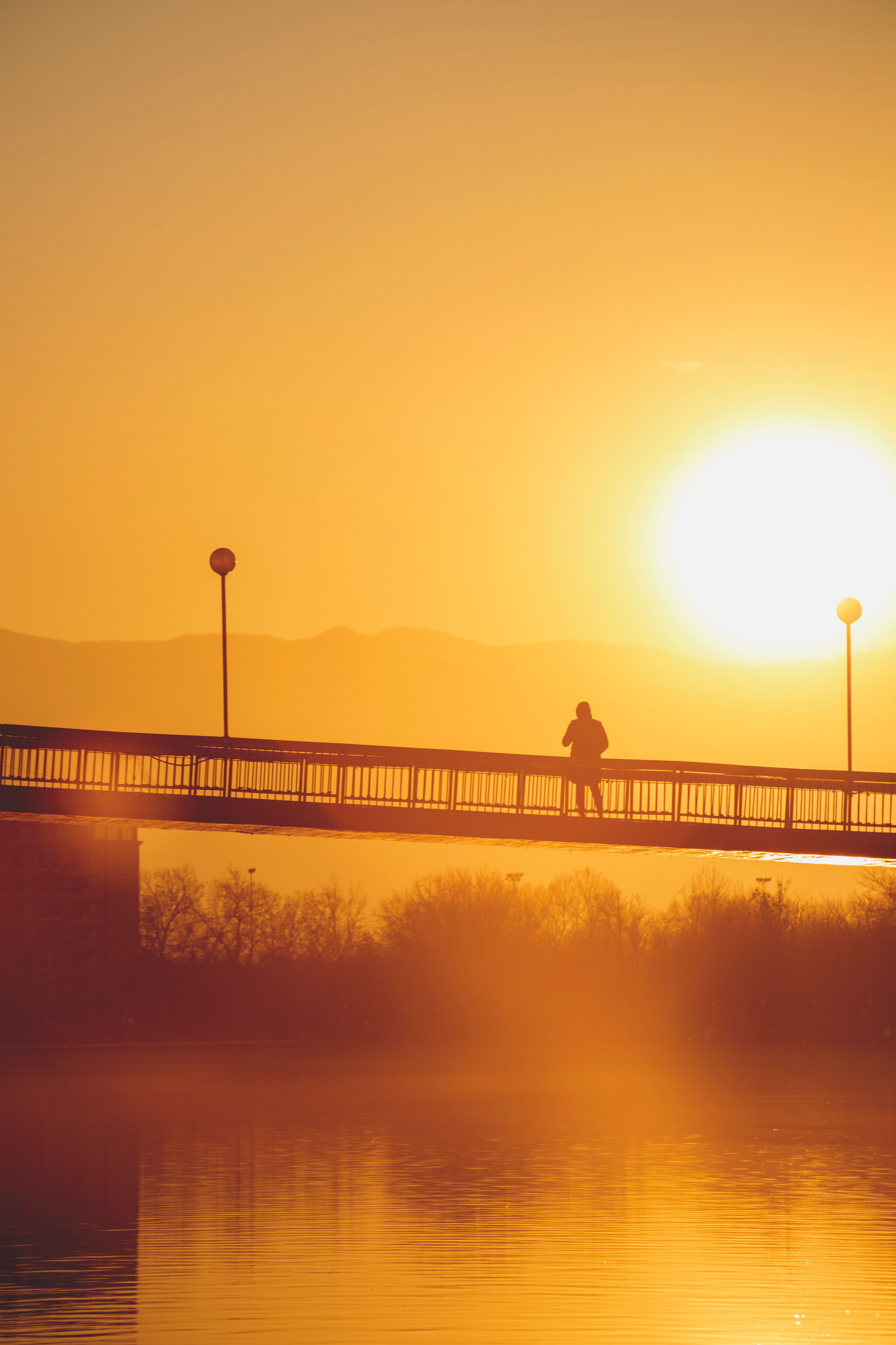 Silhouette of Person Standing on Bridge During Sunset · Free Stock Photo
