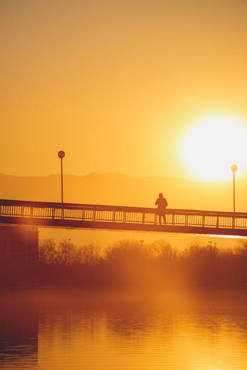Silhouette of Person Standing on Bridge During Sunset