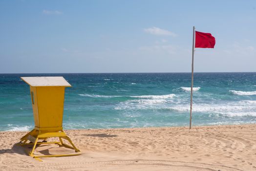 Beach scene with lifeguard station and red flag warning against strong waves.