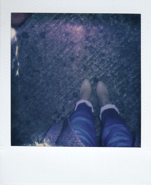 Artistic Polaroid photograph of feet in boots and jeans on textured ground.