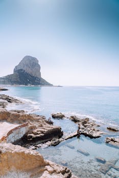 Breathtaking view of Calpe's rocky shoreline and iconic Peñón de Ifach illuminated by clear skies.