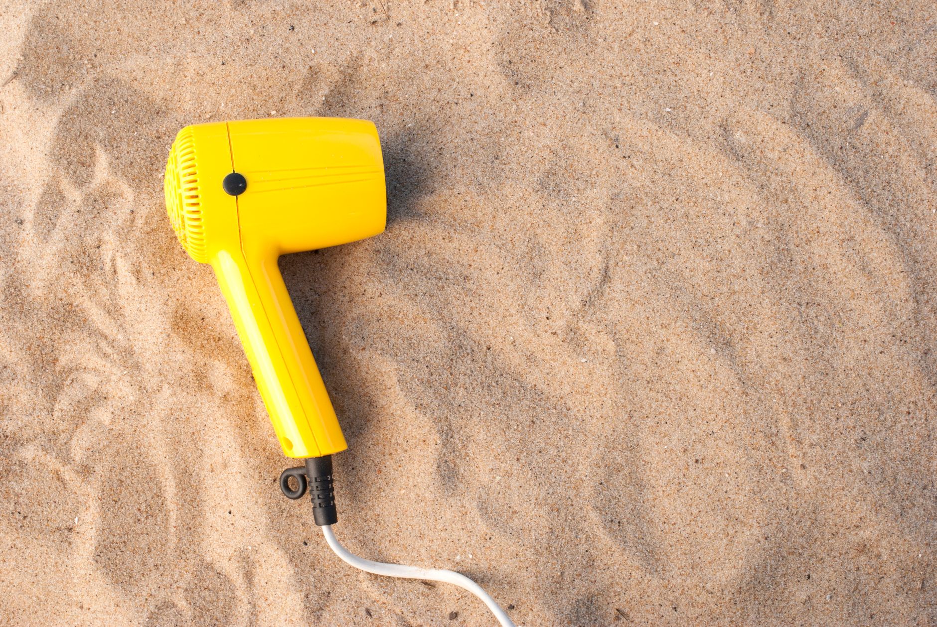 A yellow hair dryer resting on smooth sand, captured in a high angle shot.