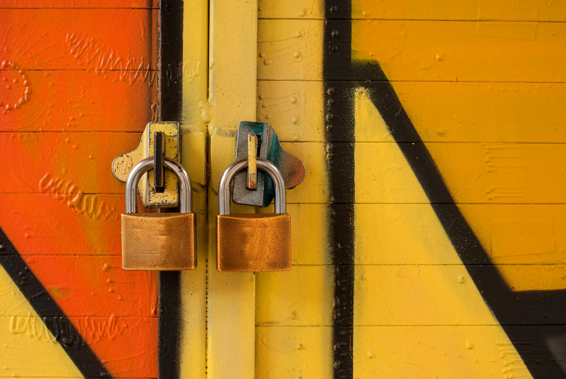 Close-up of two brass padlocks securing a vibrant graffiti-painted door, symbolizing security.