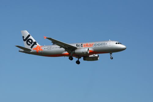 Free Jetstar Airbus A320 aircraft flying against a clear blue sky. Captured outdoors. Stock Photo