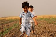 Boys Running on the Brown Loam Soil with Green Grass