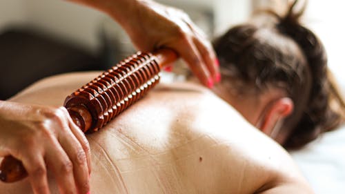 Hands Using a Wooden Massage Roller on the Person's Back 