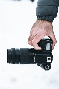 Photographer holding DSLR camera with zoom lens in snowy outdoor setting, close-up view.