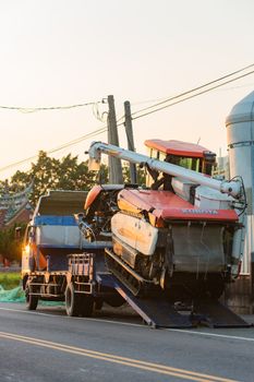 Orange excavator being loaded onto a truck in a rural setting during daytime.