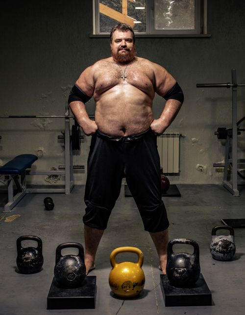 Free Muscular man shirtless in gym with kettlebells showcasing strength. Indoor workout concept. Stock Photo