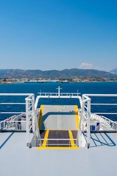 A ferry ramp leading to the bright blue waters of Patras, Greece, with scenic mountains in the background.