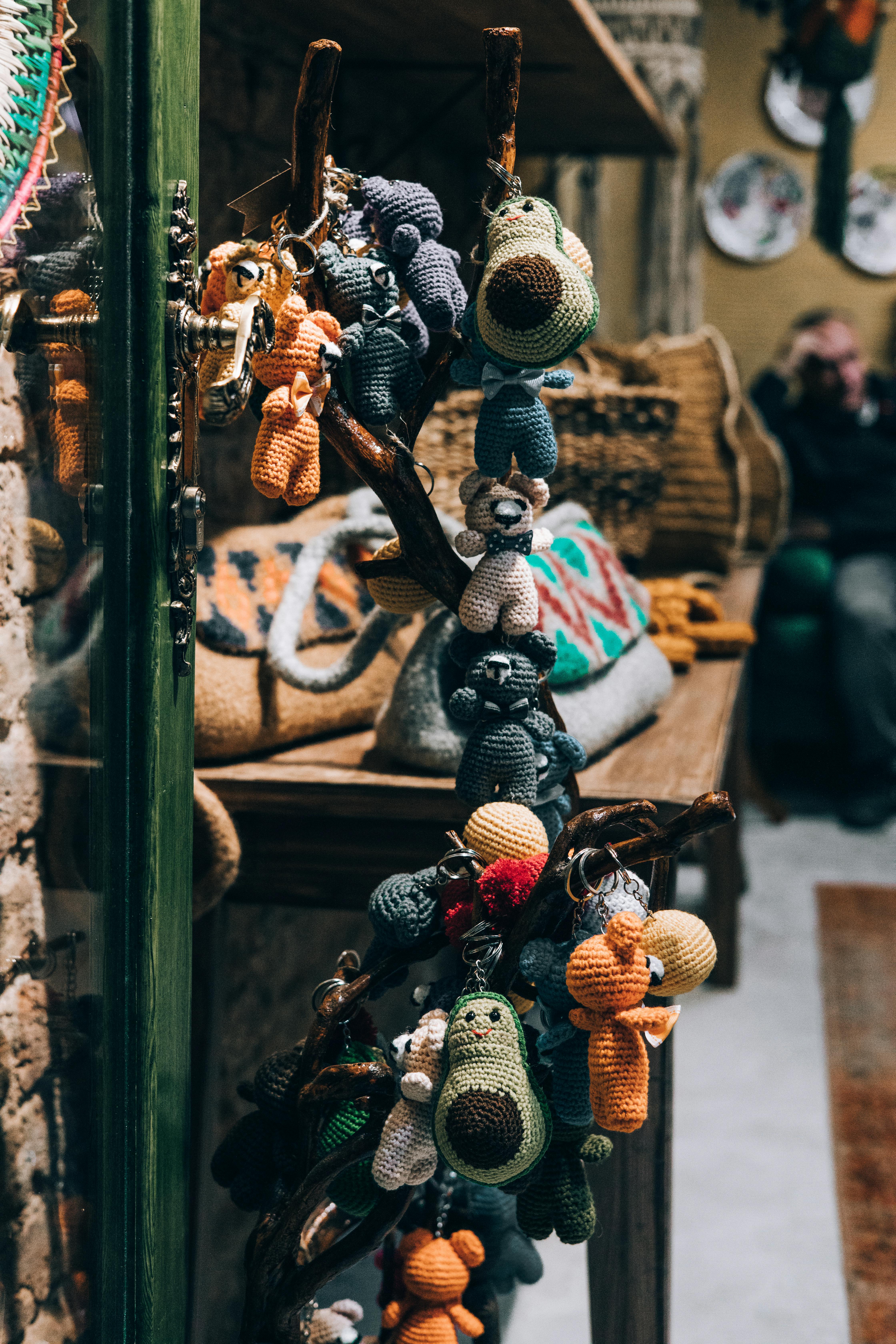 Colorful handmade crochet toys hanging from a rack in a cozy retail store setting.