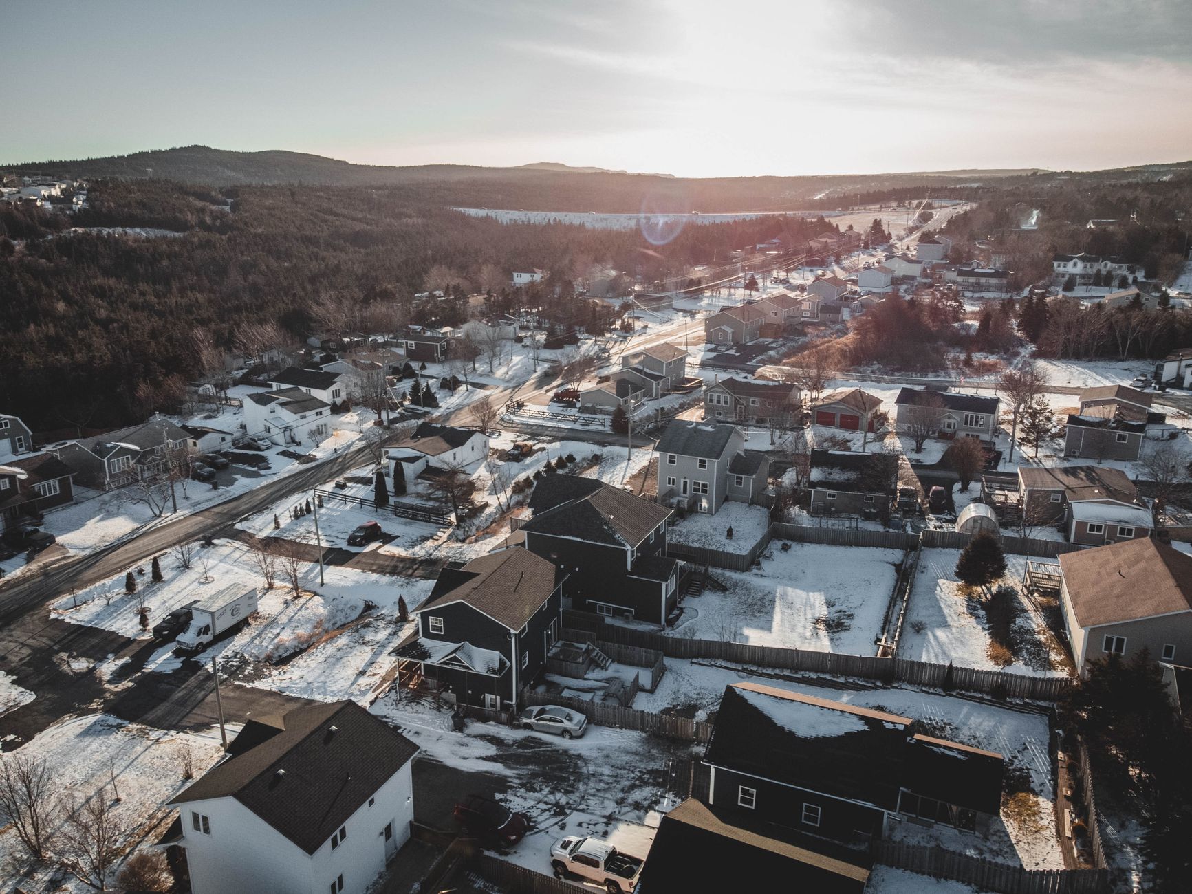Drone shot of a snowy residential area with houses and streets in winter sunlight.