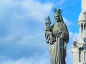 Bronze statue of Madonna and Child with crowns against a blue sky at Sainte-Anne-de-Beaupré Basilica.