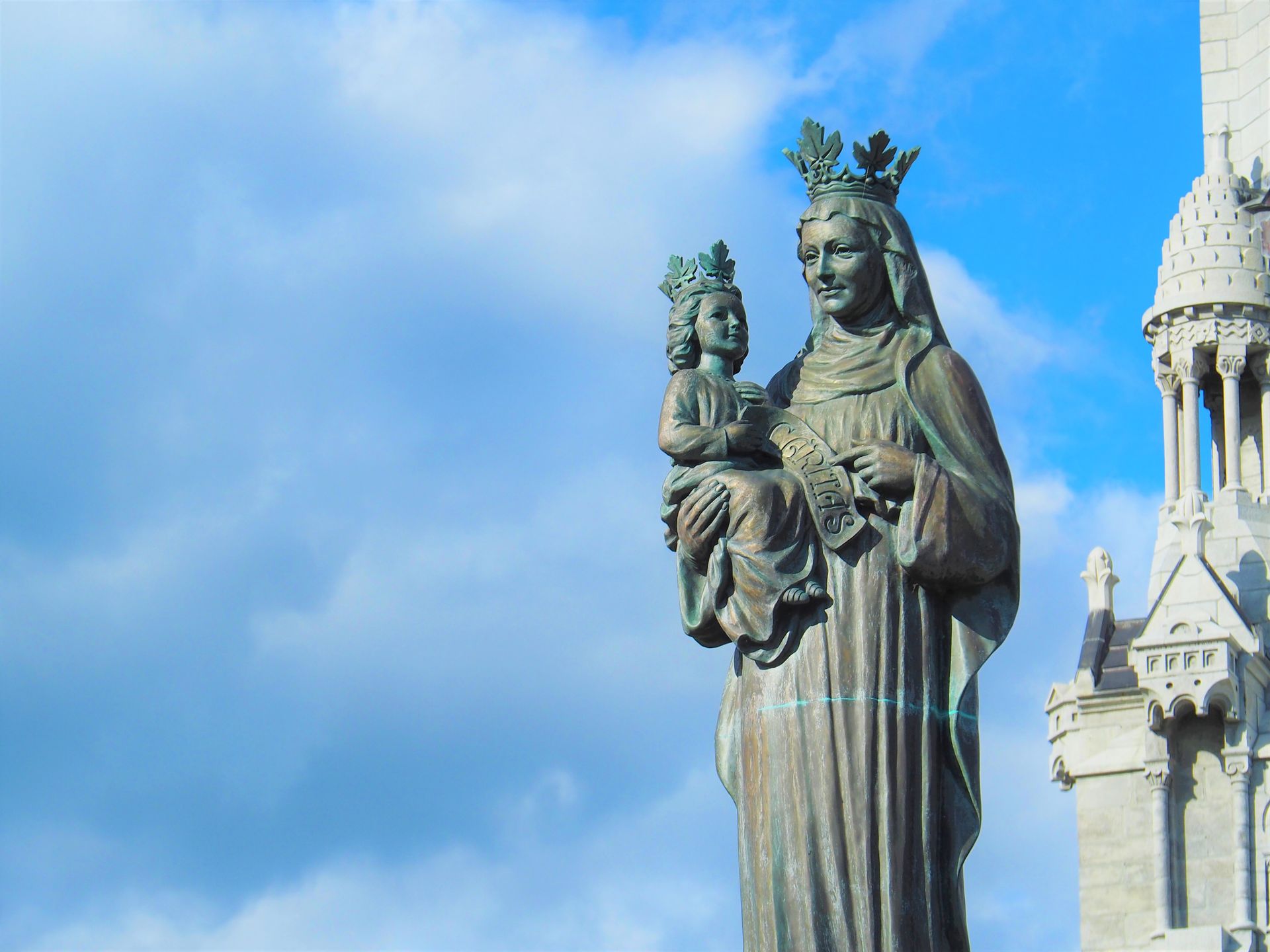 Bronze Virgin Mary Statue Covered with Green Patina, against Blue Sky