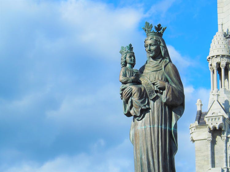 Bronze Virgin Mary Statue Covered With Green Patina, Against Blue Sky