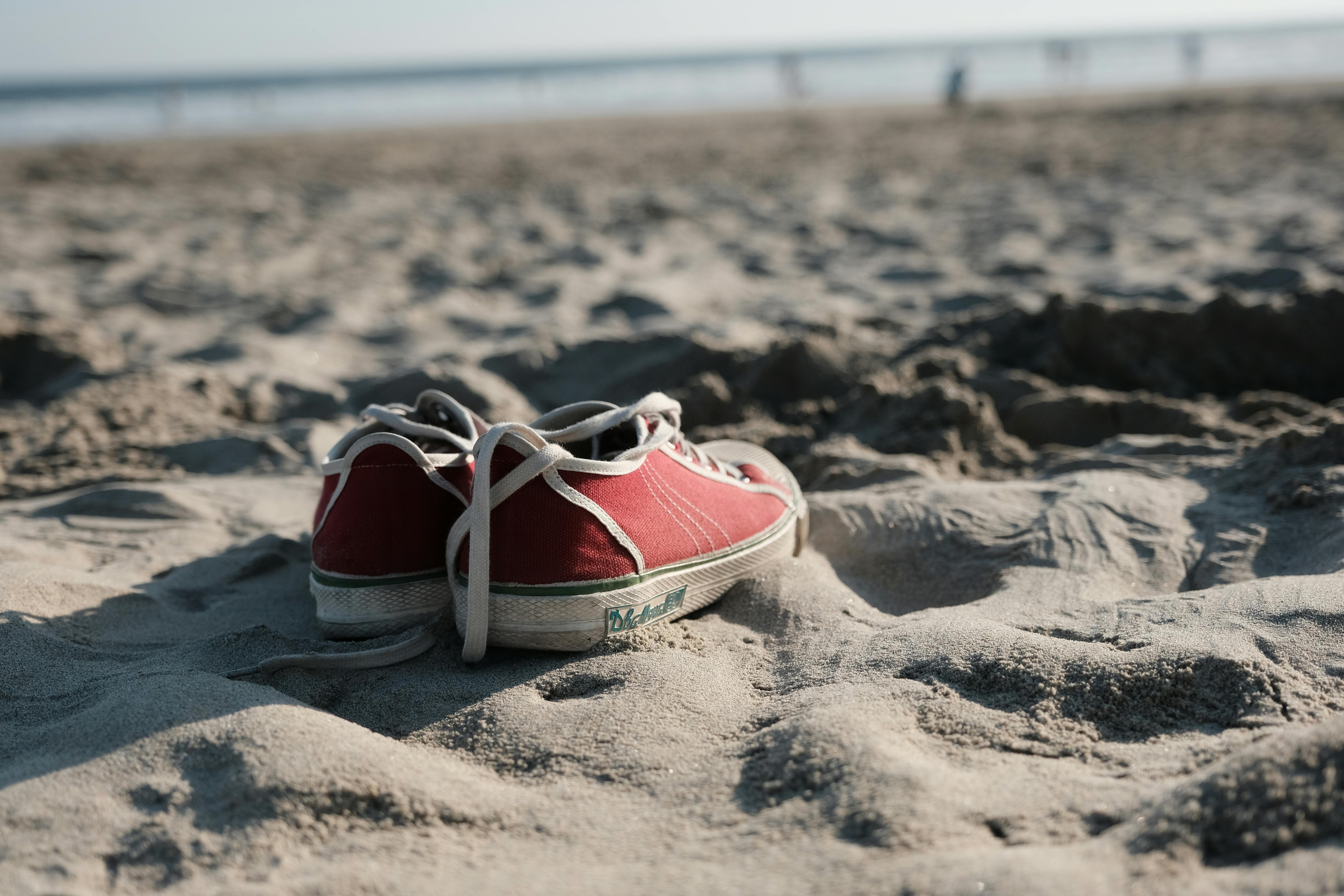 Casual red sneakers on a sandy beach, evoking a relaxed summer vibe.