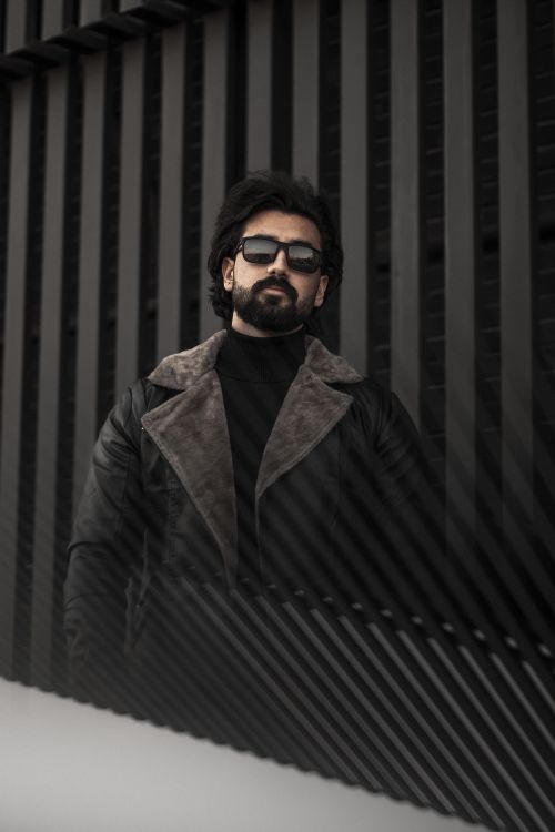 Free Confident man in sunglasses and leather jacket posing against a modern urban backdrop. Stock Photo