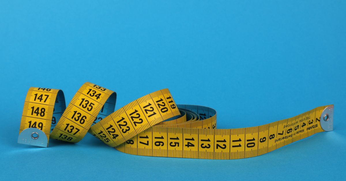 Coiled yellow soft measuring tape lying on a flat blue background