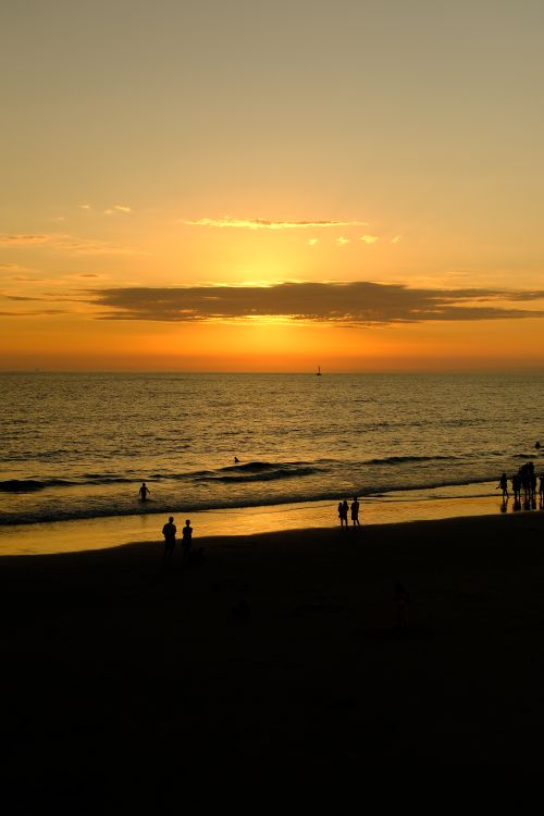 Free Captivating beach sunset with people silhouetted against the golden sky and ocean waves. Stock Photo