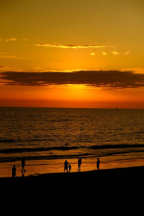 Free Silhouettes stroll along a serene beach during a vibrant golden hour sunset. Stock Photo