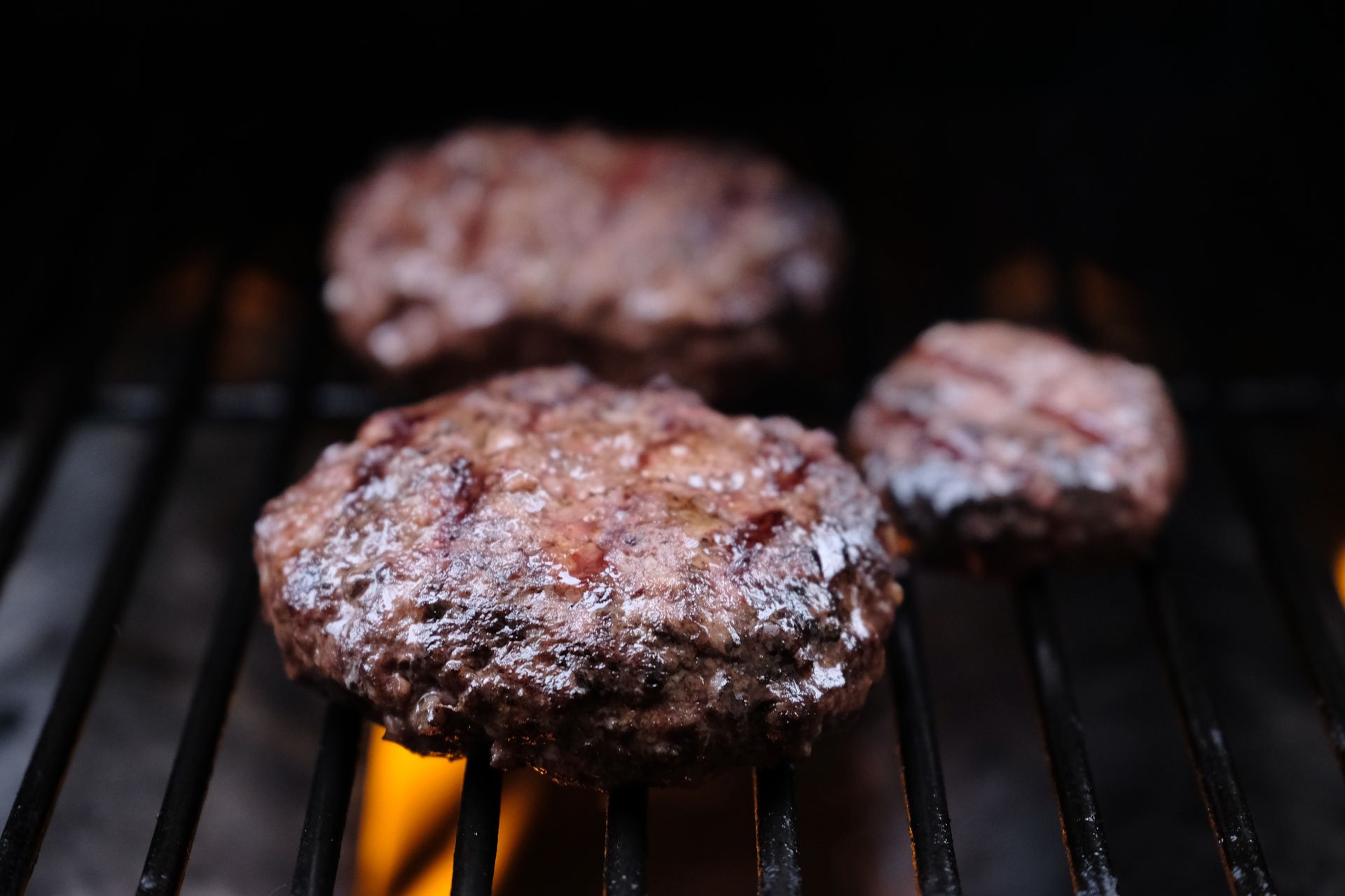 Close-up of savory burger patties sizzling on a grill, perfect for barbecue enthusiasts.