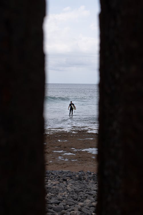 Person Walking on Beach Holding a Surfboard