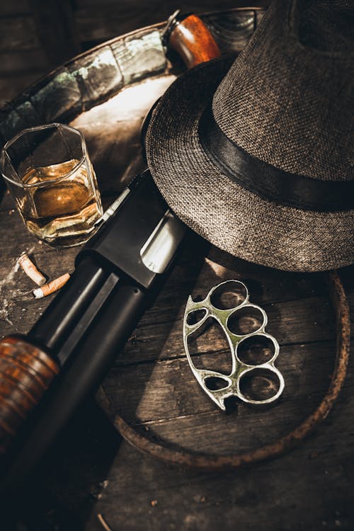 Metal Knuckle Duster Beside Fedora Hat and Whiskey Glass
