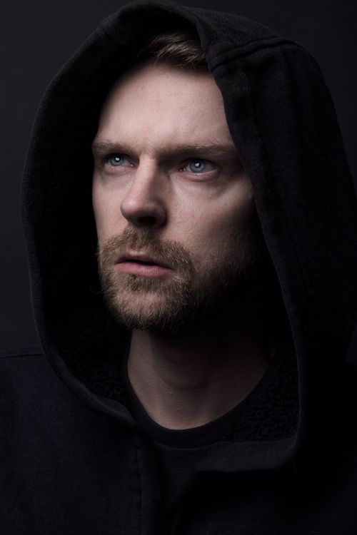 Free Close-up of a man with a hood looking upward in a dramatic, moody light. Stock Photo