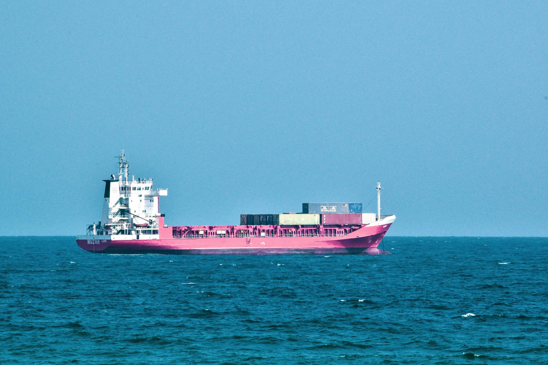 A vibrant pink cargo ship sails through calm blue ocean waters under a clear sky.