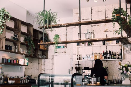 Free Charming rustic café interior with lush plants and a barista at work, featuring a vintage vibe. Stock Photo
