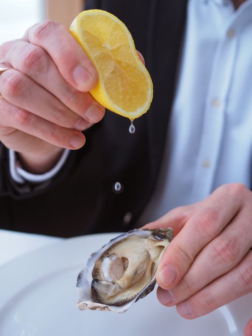 Free Close-up of hands squeezing lemon juice on an oyster, enhancing gourmet seafood dish. Stock Photo